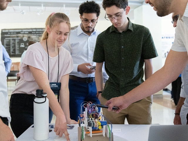 Students gather indoors and work on a project that is sitting on a table